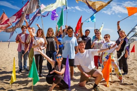Photo of a group of people on a beach waving colourful flags